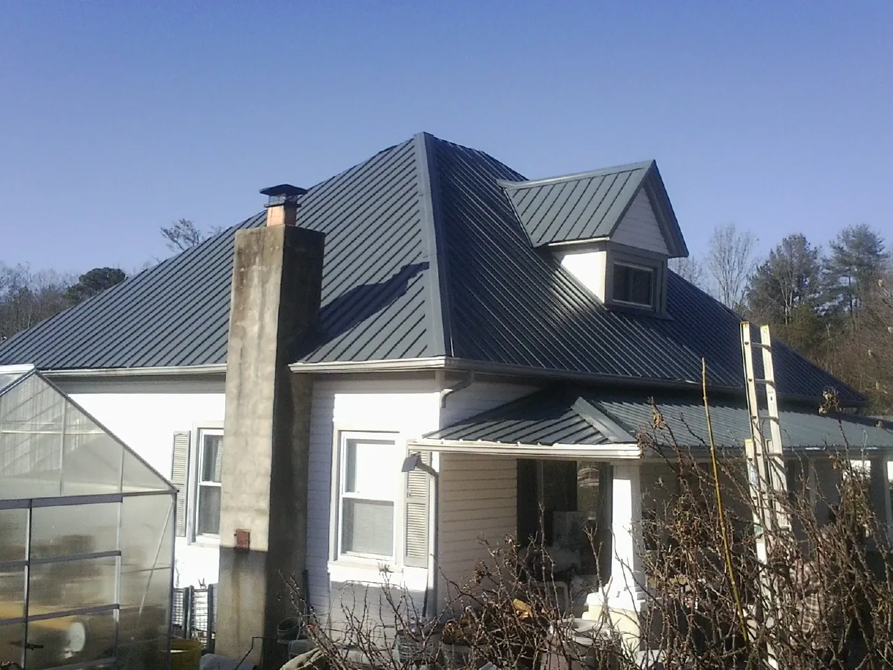 Dark blue standing seam metal roof on a white farmhouse with dormer — Slate & Tile Roof Repair by Roofing Brothers in Howe