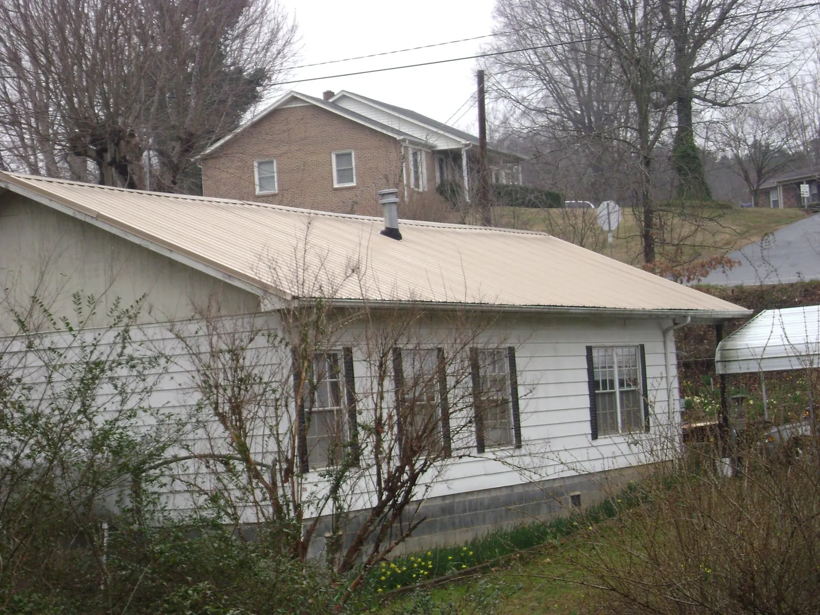 Tan metal roof on a white sided house set into a hillside — Commercial Roofing by Roofing Brothers in Howe