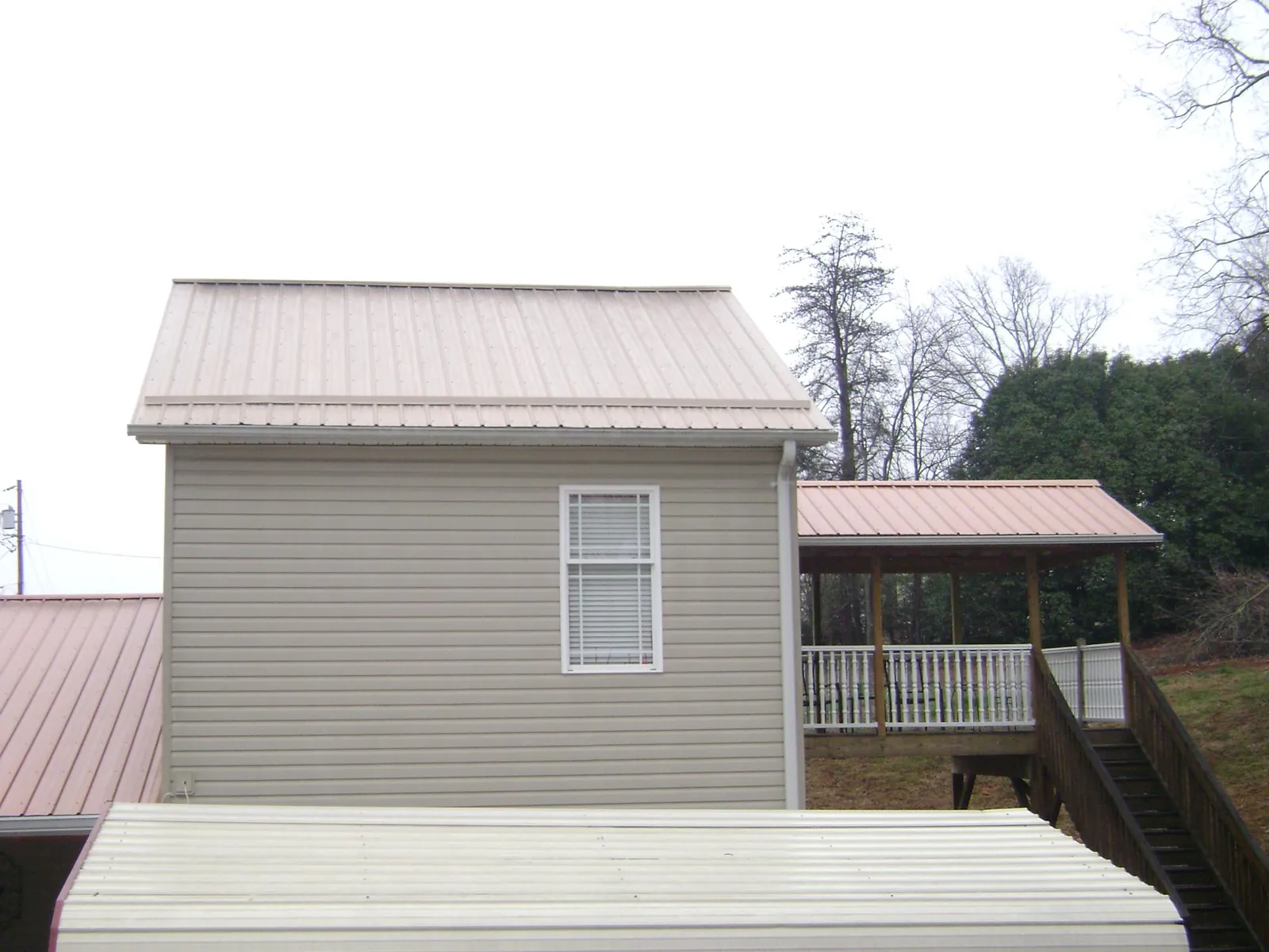 Tan metal roofs on a two story addition and attached porch, from a Roof Replacement job in Howe